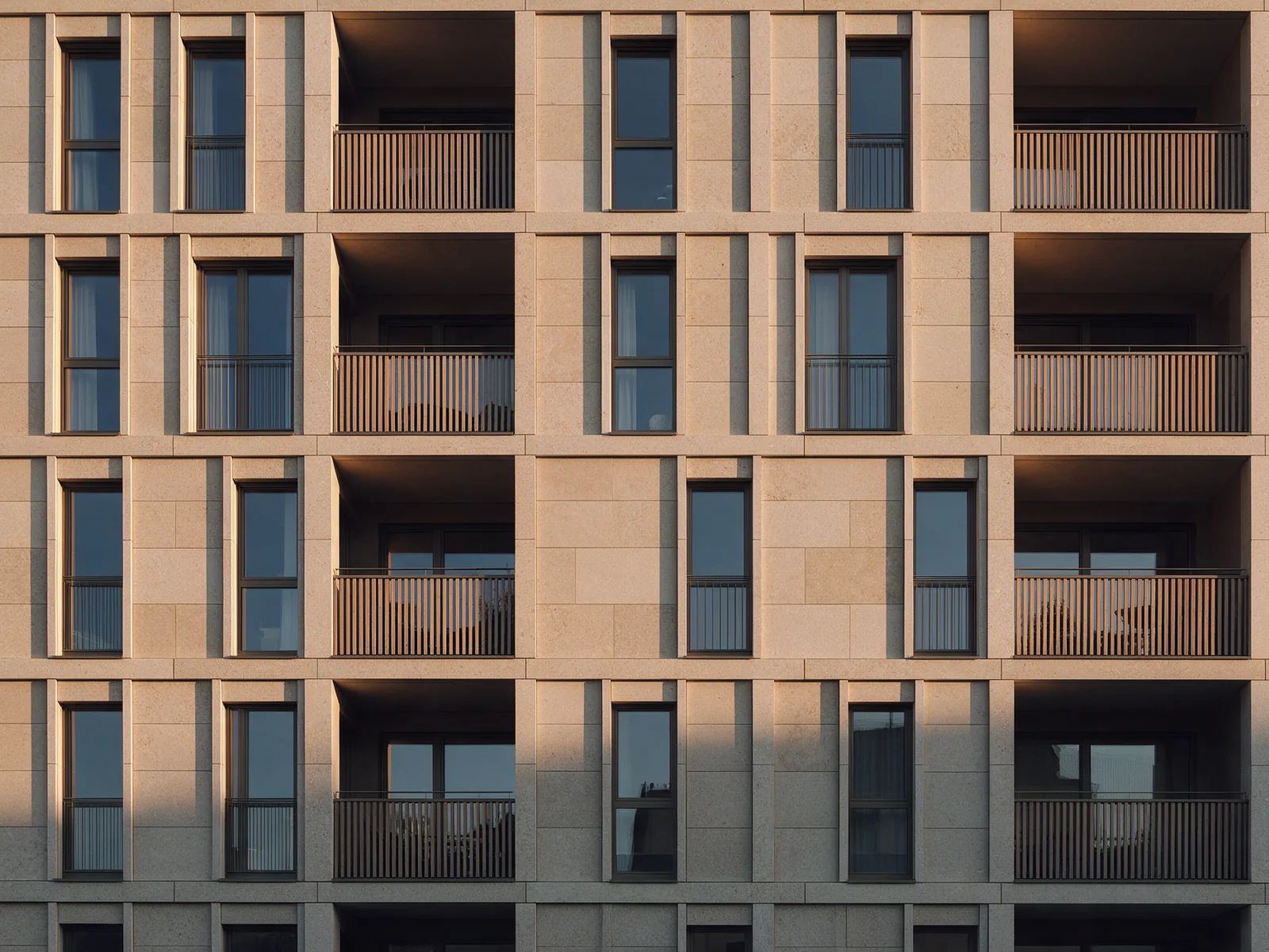 Façade d'immeuble en pierre beige, fenêtres et balcons en bois sous la lumière du soir